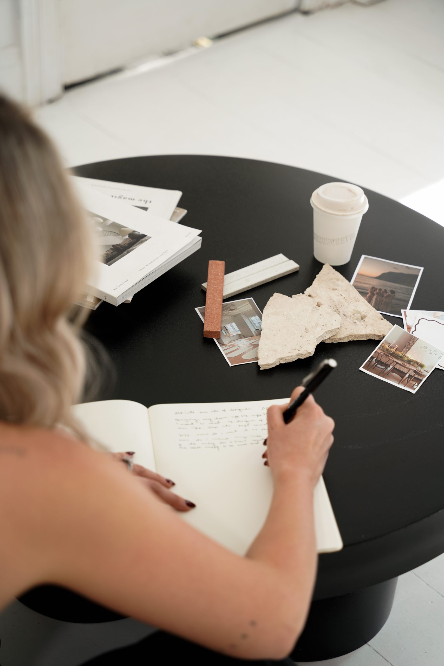 Overhead view of hands writing in a journal surrounded by photos, tile samples and magazines