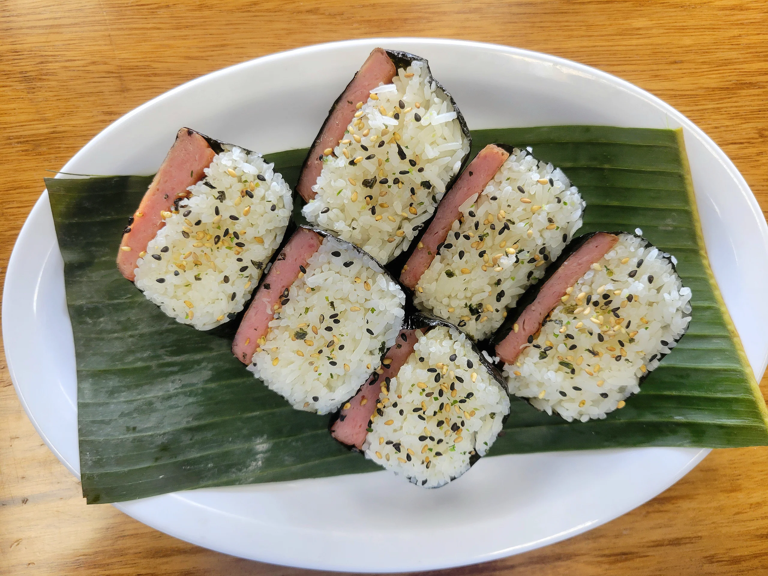 Three pieces of Hawaiian Spam Musubi with teriyaki glaze and furikake on a green banana leaf.
