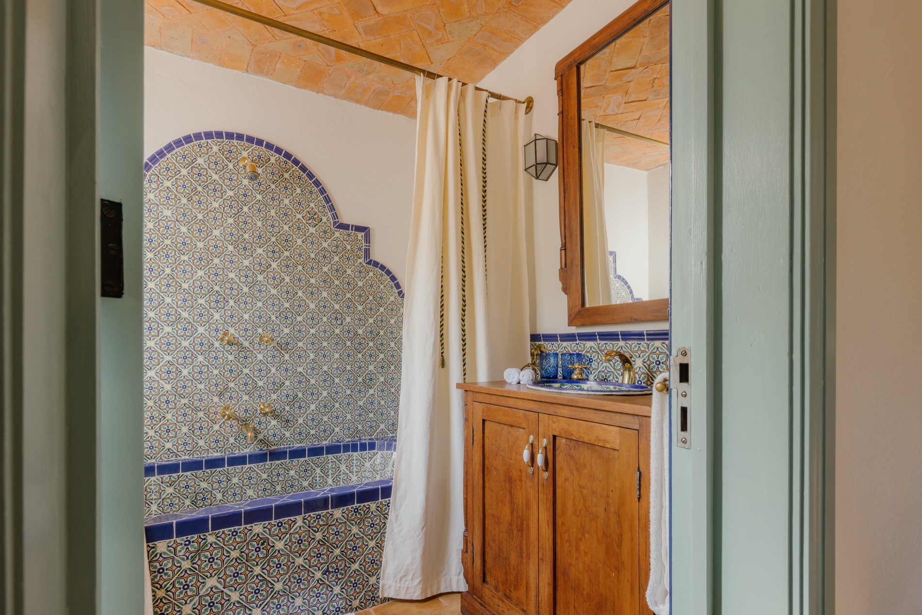 La Residencia bathroom with arched tile shower niche, brick ceiling, and painted sink