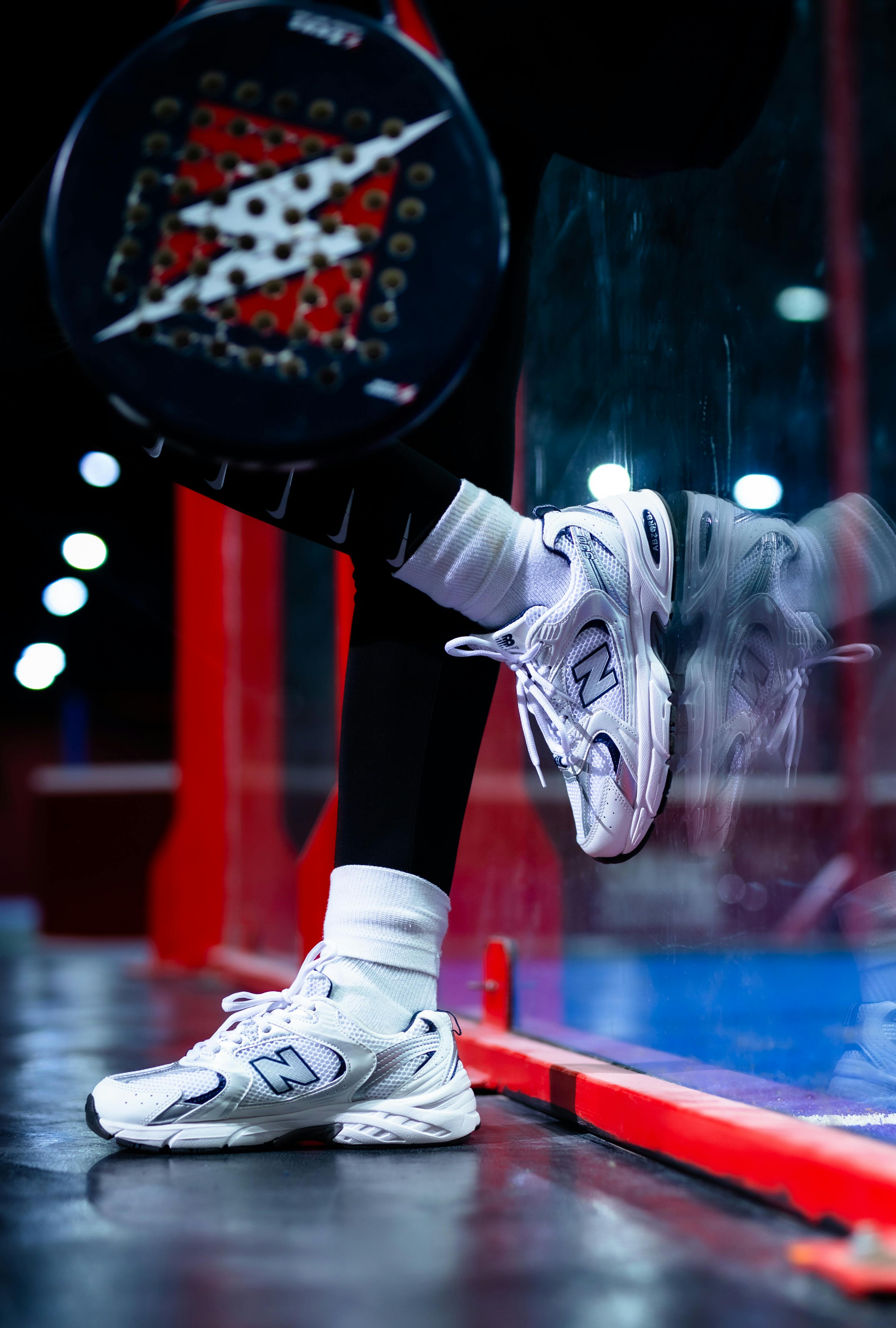 A young person with curly hair smiles at the camera while sitting in front of a laptop against a dark background.