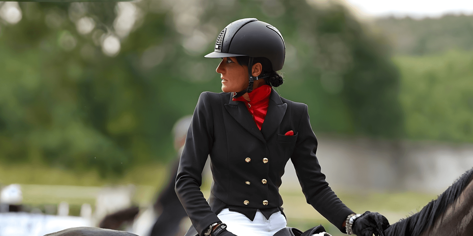 A woman in an equestrian outfit with a red accent, riding her horse, embodying style, presence, and authority in competition.