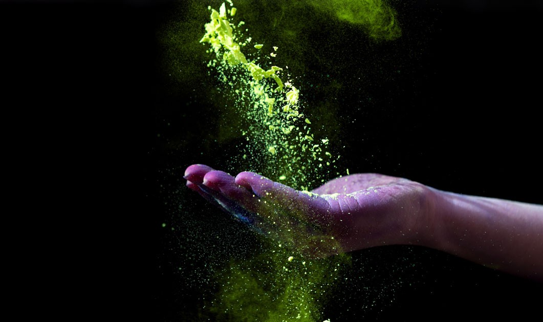 Żółty proszek holi spadający na dłoń oświetloną fioletowym blaskiem na czarnym tle