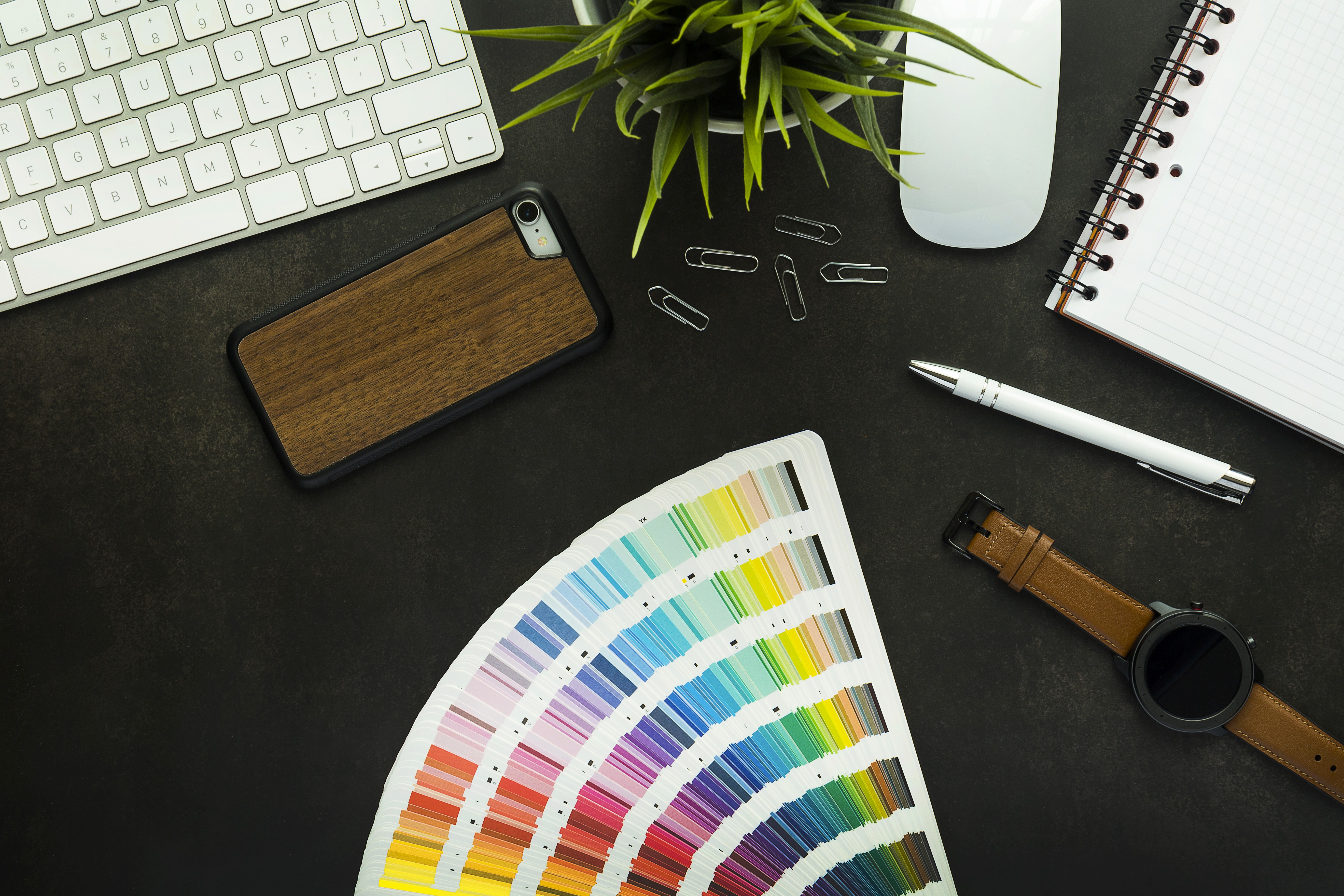 Top view of a modern designer workspace with color swatches, keyboard, smartphone, notebook, and pen on a black desk