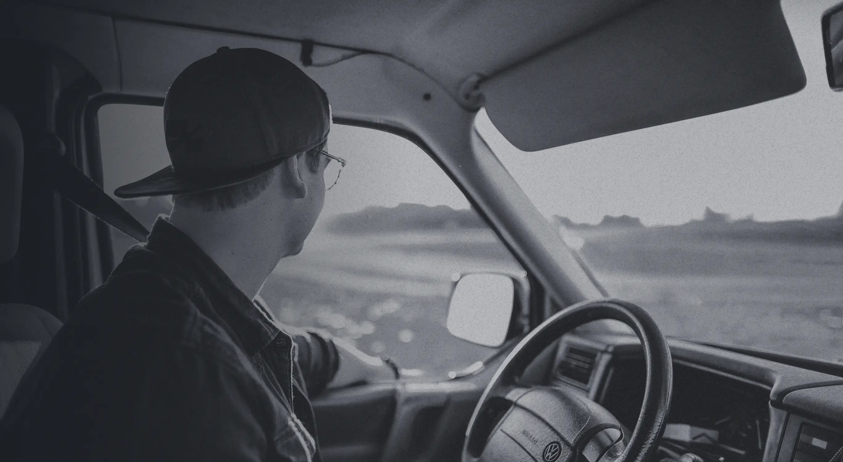Close-up of a truck driver behind the wheel driving and looking out his window at the landscape on a clear day