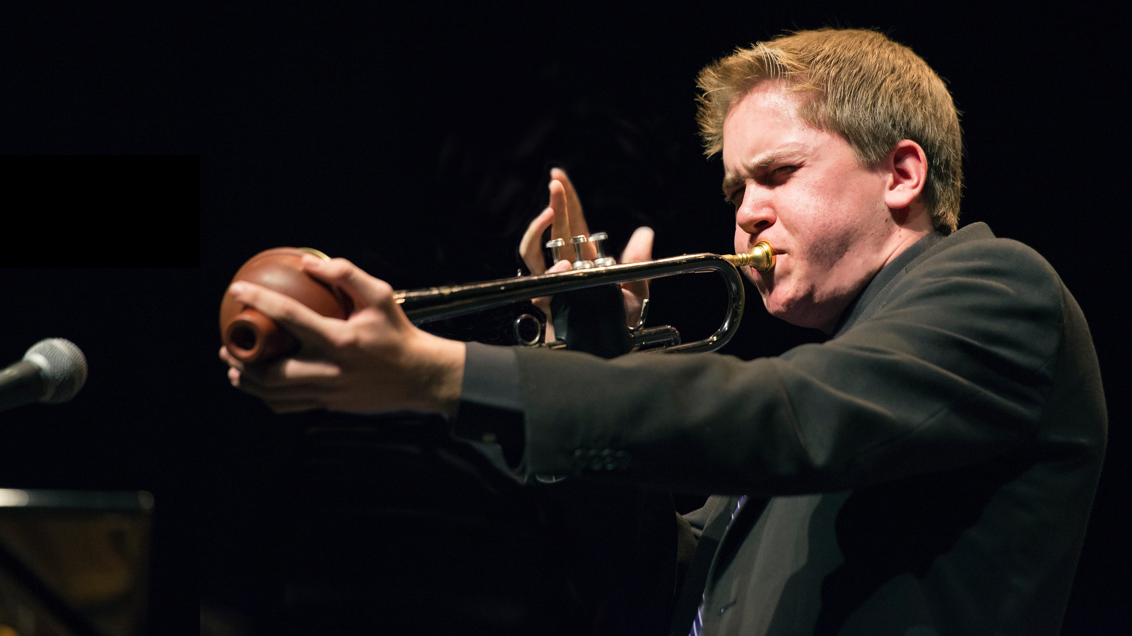 Alex playing trumpet holding a plunger mute to the trumpet bell
