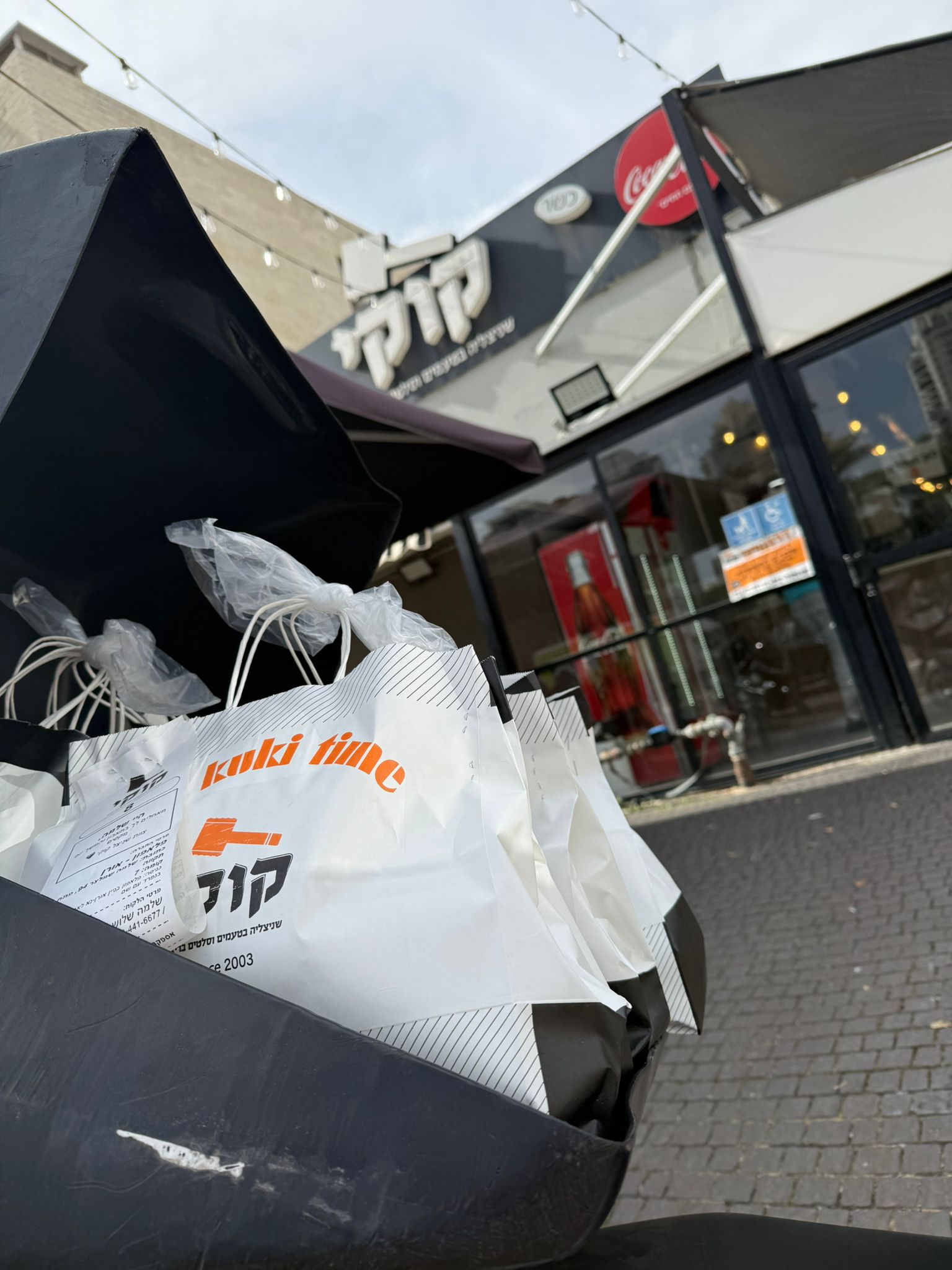 שקיות משלוח מונחות בקופסת אופנוע מחוץ למסעדה.