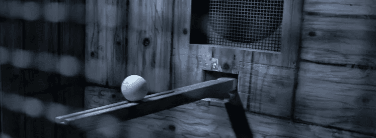 A young person with curly hair smiles at the camera while sitting in front of a laptop against a dark background.