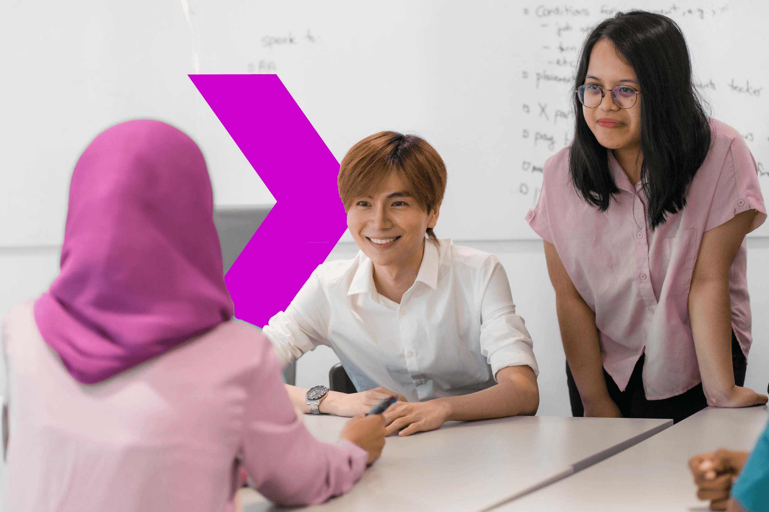 A group meeting is in progress at a table, with two individuals in pink attire engaged in discussion, and a large purple arrow on the wall.