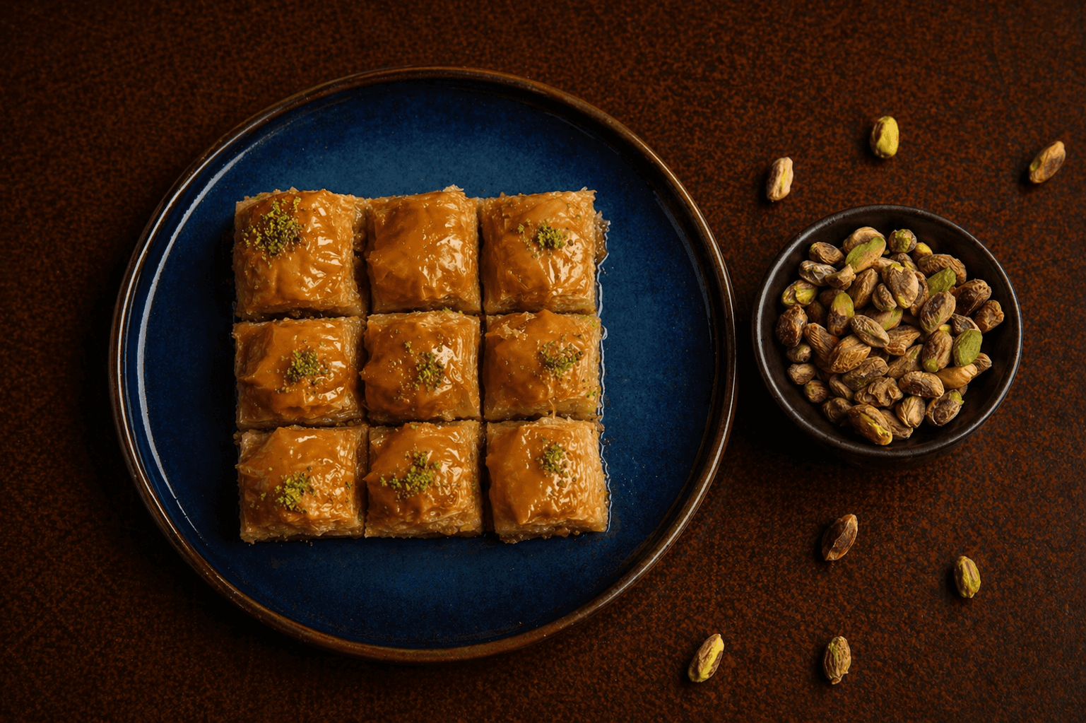 Baklava layered with flaky phyllo, chopped pistachios, and syrup on a dark blue plate at Café Sherpa's café in Brookfield, WI. A sticky, rich Middle Eastern classic.