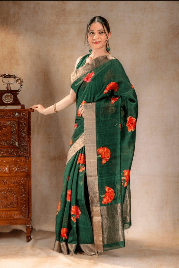 A woman wearing a green Dupion silk saree from That Saree Shop, featuring elegant golden borders and delicate orange floral prints, blending textured luxury with vibrant handcrafted detail.