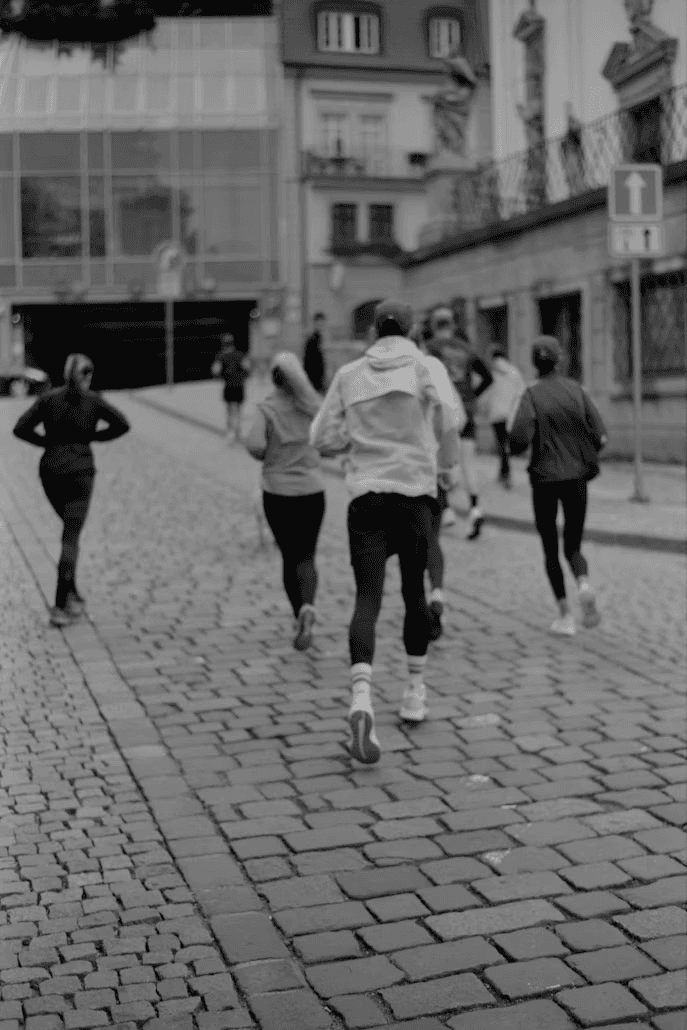 Black and white image of people walking on a cobblestone street, with buildings in the background.