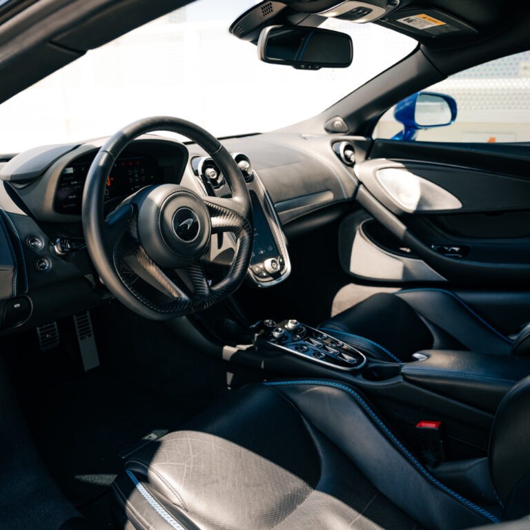 Interior view of the blue McLaren GT's driver's seat and dashboard, highlighting the luxurious cabin.