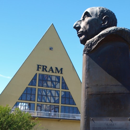 Треугольное желтое здание с надписью "FRAM" с большими окнами и бюстом мужчины на переднем плане.