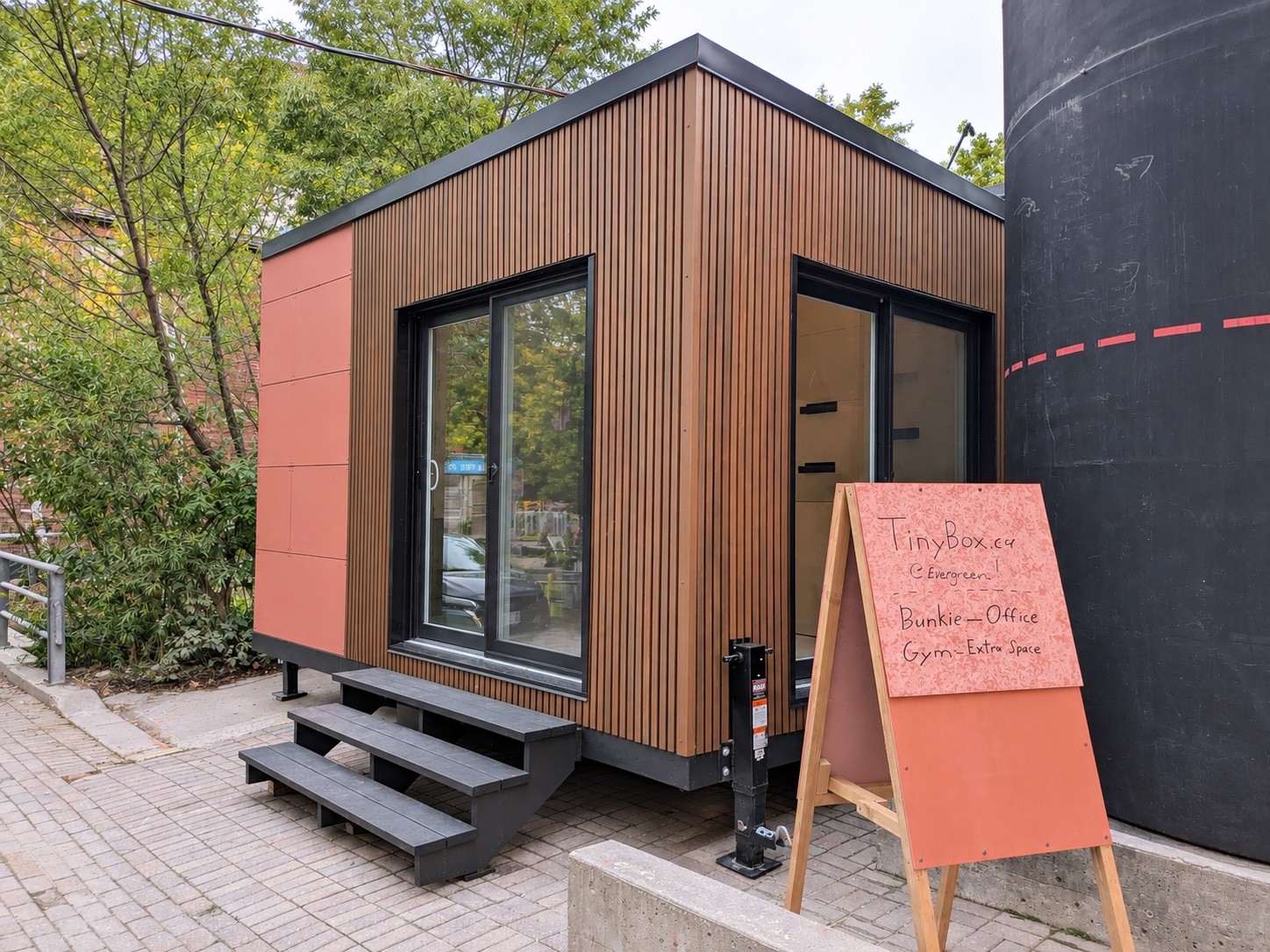 Tinybox at Evergreen Brick Works, with wood cladding, glass doors and entry steps beside the original industrial silo.