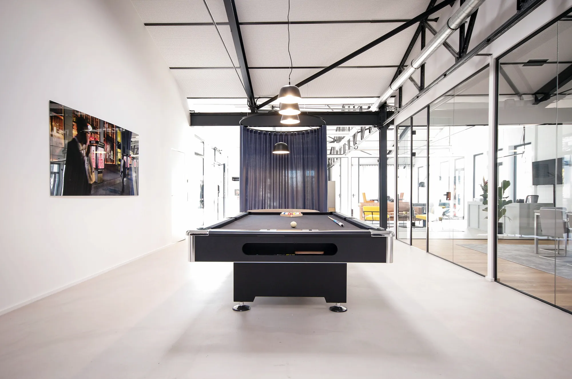 Black pool table under pendant lights with a street photograph on the white wall.