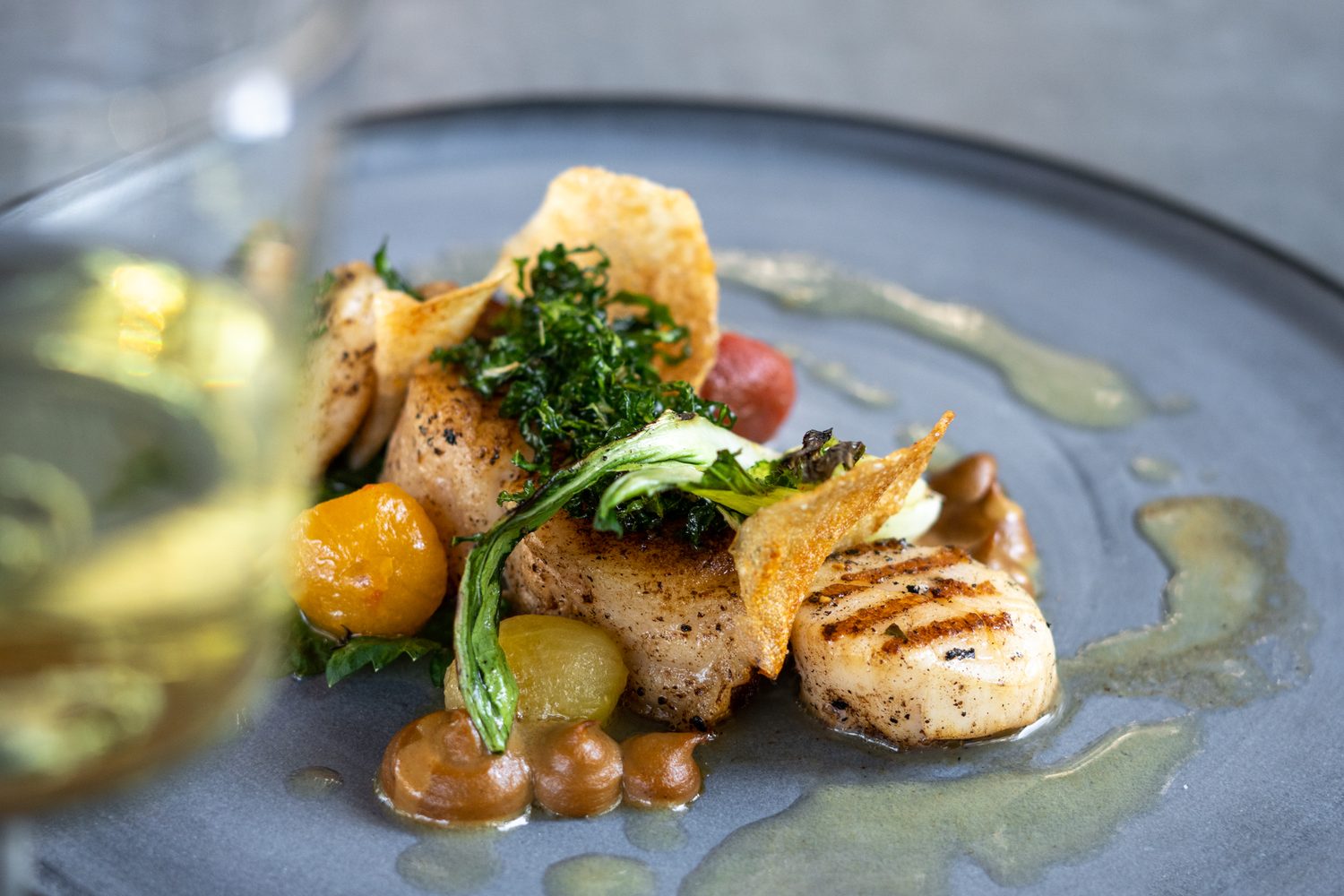 A finely plated course with a glass of white wine beside it