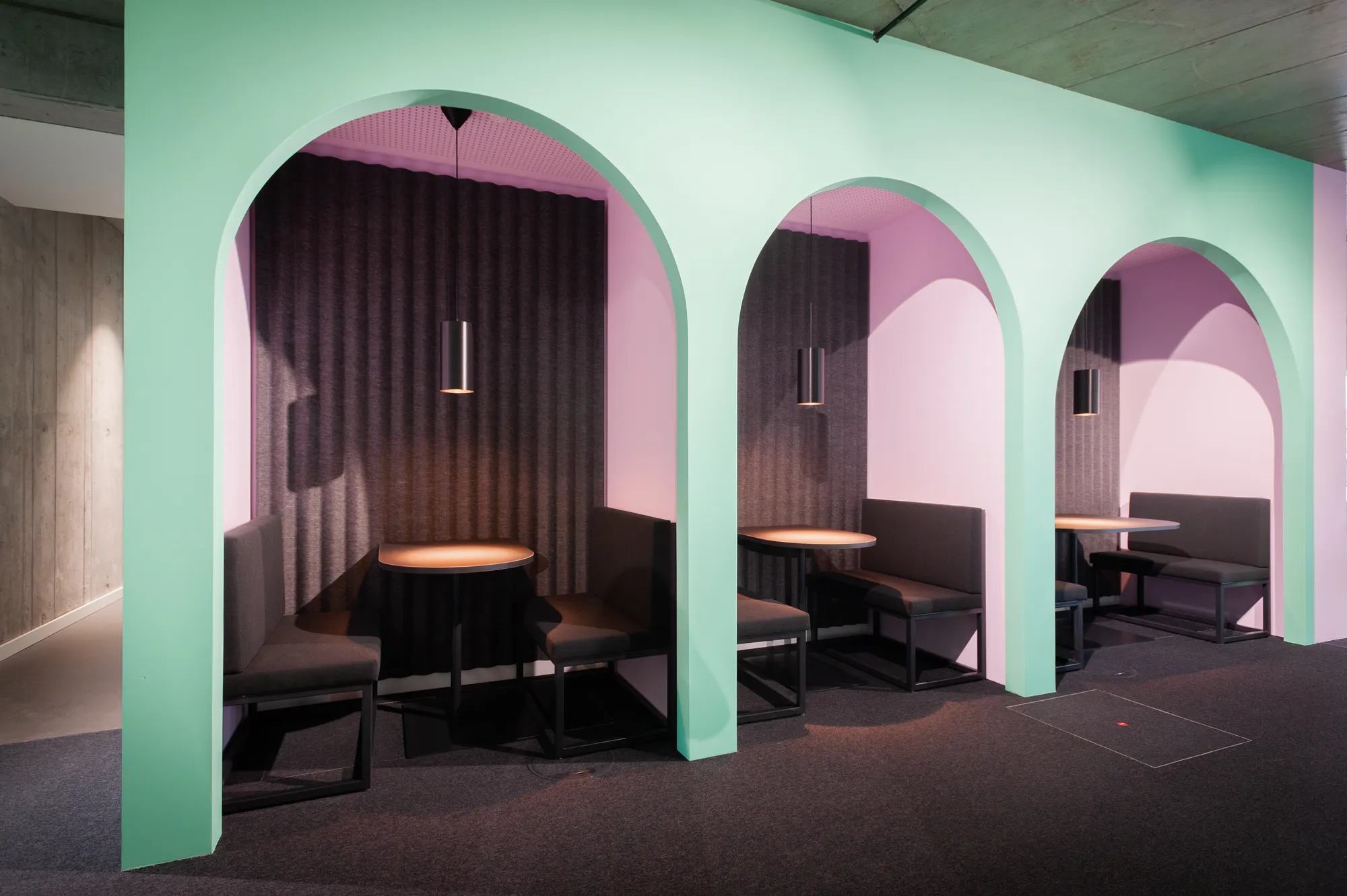 Green arched booths with upholstered benches, round tables and pendant lights.