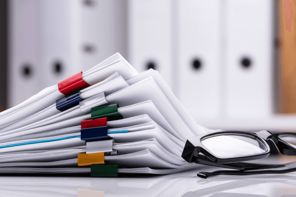 stacked documents with colorful paperclips and eyeglasses