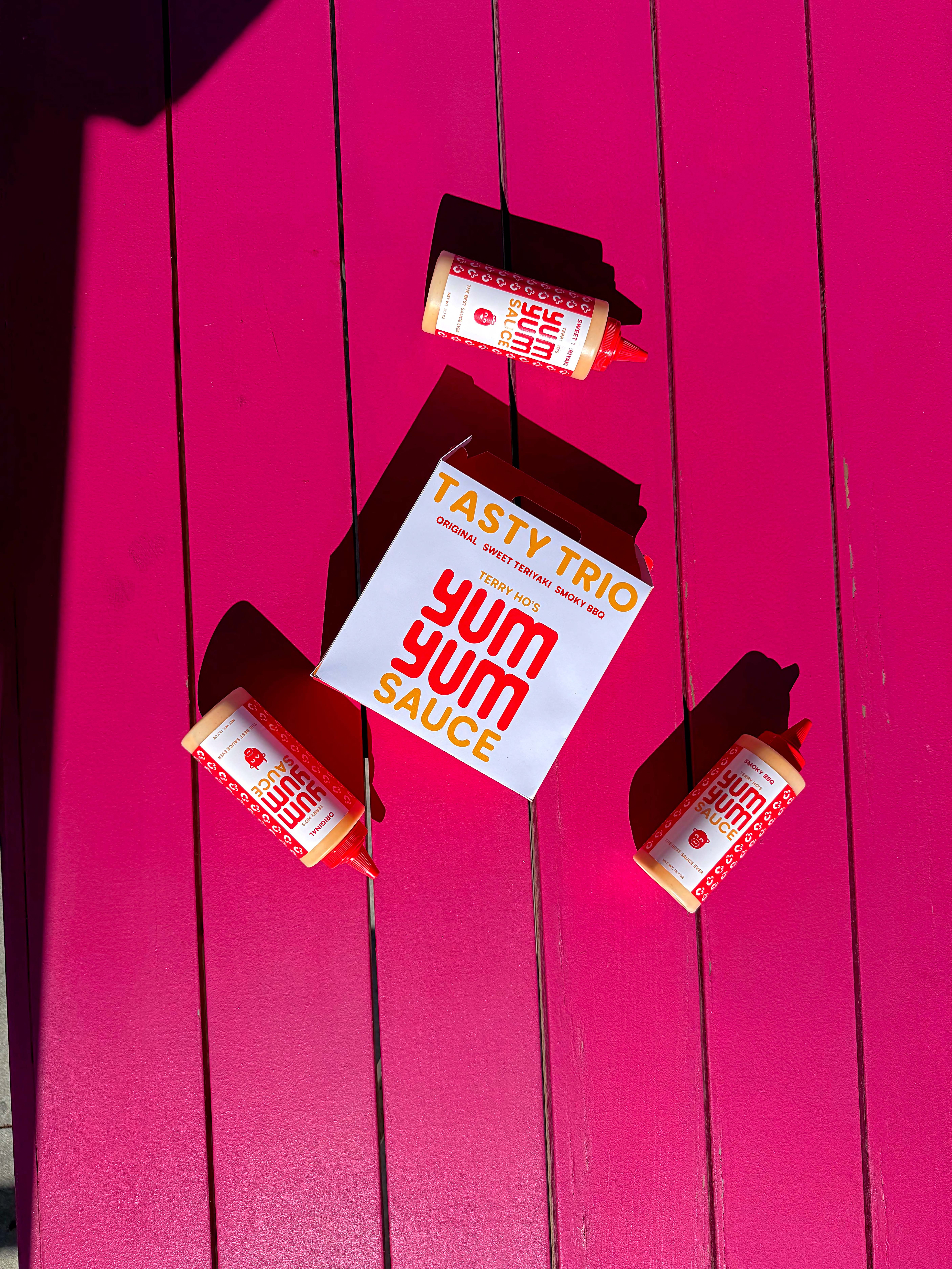 Dipping sauce trio box laying down on a pink picnic table with squeeze bottles of suace surrounding it