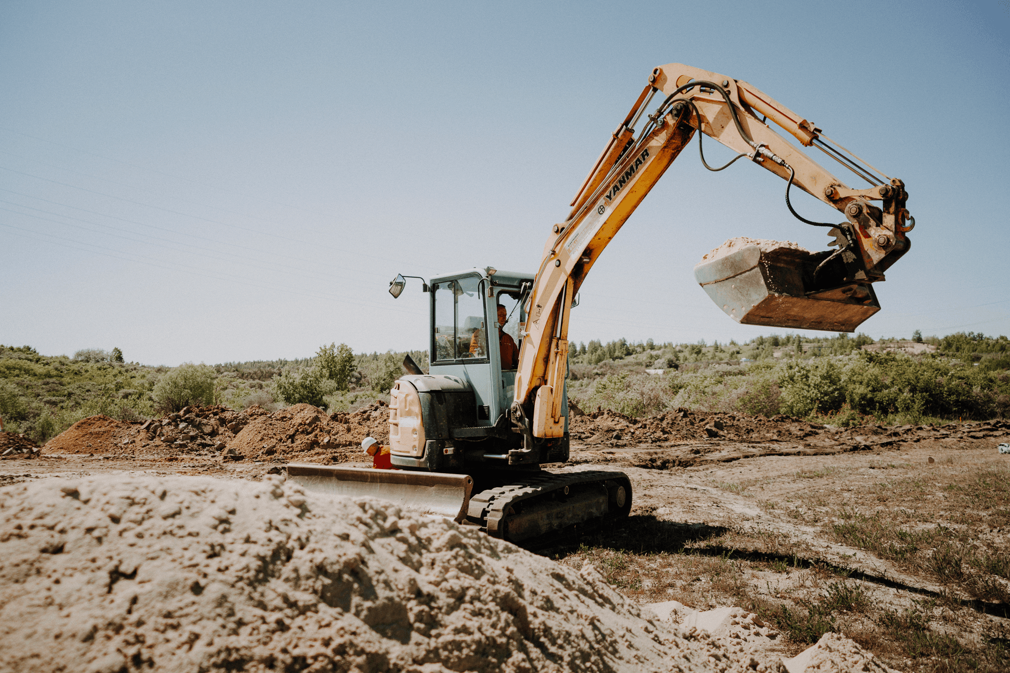Ein Bau-Bagger mit angehobenem Arm gräbt auf einer Erdbaustelle unter einem klaren blauen Himmel.