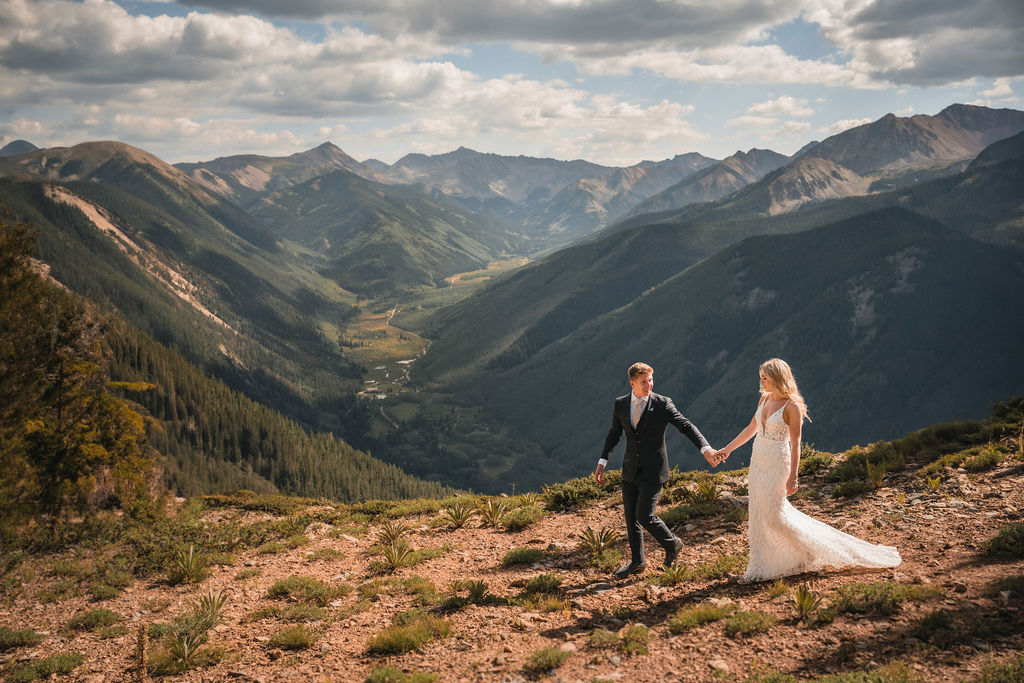 Bride and groom walking along ridge at Smith Cabin Aspen wedding with sweeping mountain views