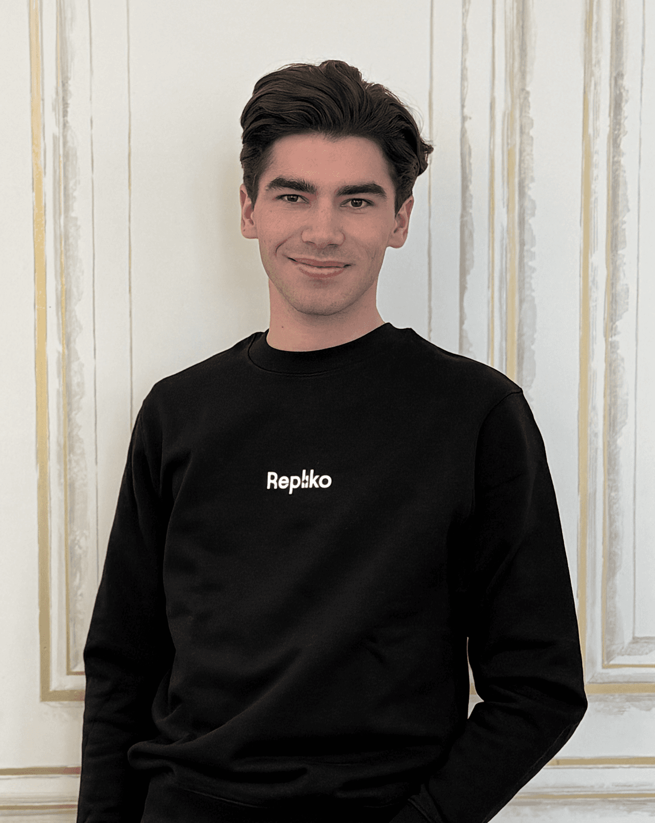 Smiling young man with curly hair, wearing a dark hoodie, against a softly lit background.
