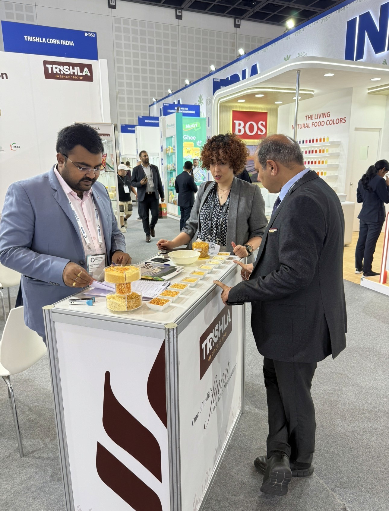 A man and woman sit on beige chairs in a modern room with a red paneled wall. A red pendant light hangs above a wooden coffee table between them.