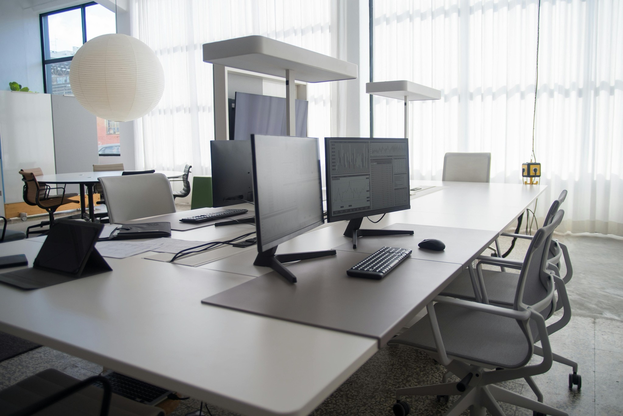 Modern, empty office desk setup. A large computer monitor displays complex financial charts and data dashboards. A mesh office chair is visible in the foreground, with the New York City Office address listed below.