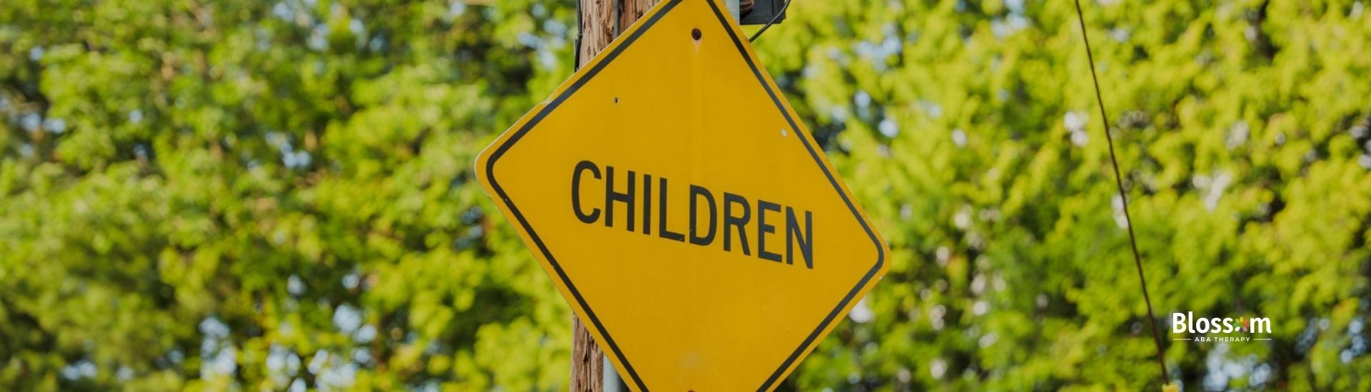 A bright yellow "Children" road sign against a backdrop of trees and a house.