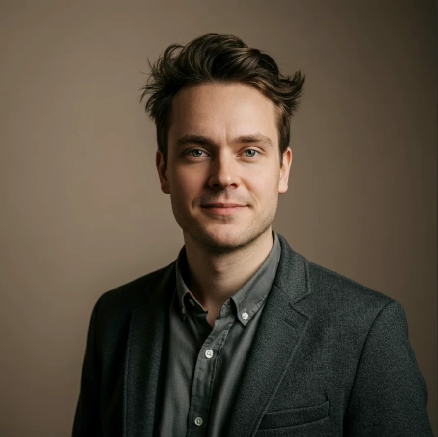 Professional portrait of a young man smiling in a dark collared shirt against a neutral backdrop.