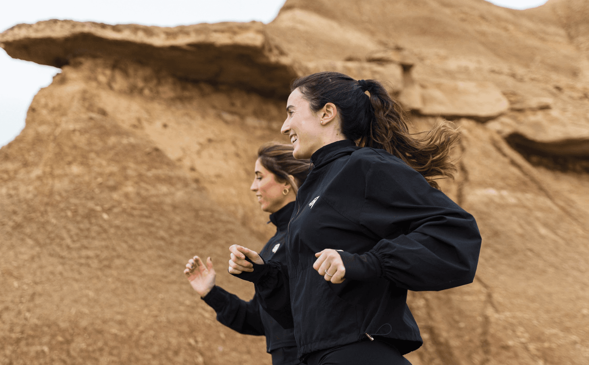 Stylish woman in a gray athletic outfit and headband standing confidently in a stadium, surrounded by empty blue seats and overhead steel beams.