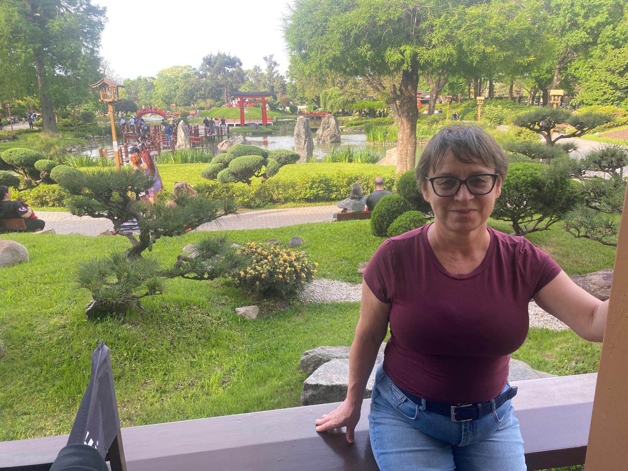 Mujer sentada sobre un tronco frente a una cascada doble en un bosque frondoso de Argentina.