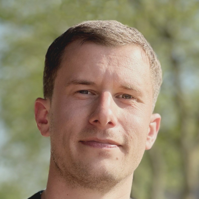 Smiling young man in a black t-shirt against a gray background, radiating warmth and friendliness.