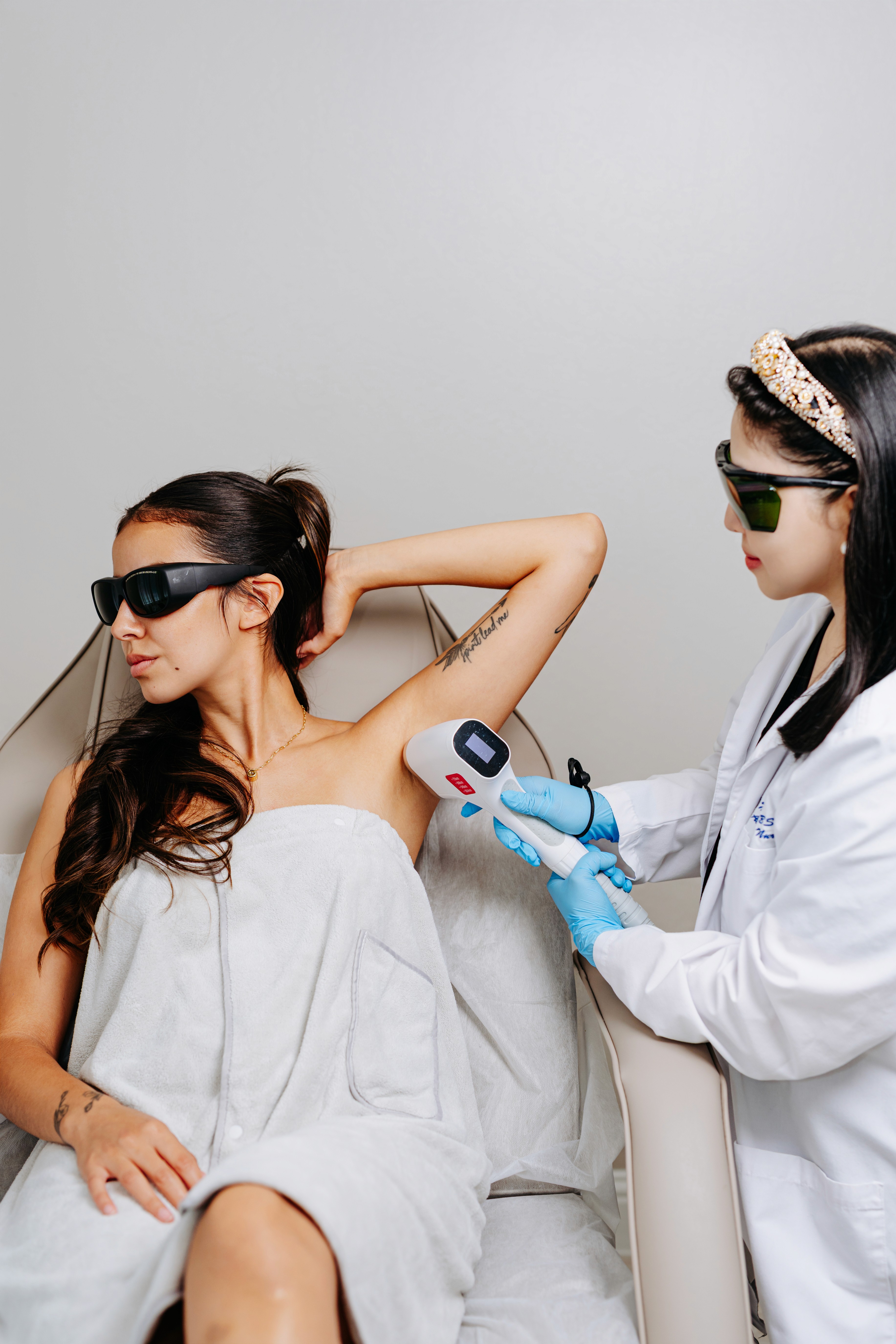 A skin professional assists a patient seated in a treatment chair in a clean, modern clinic setting.