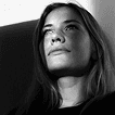 Black-and-white close-up portrait of a woman looking slightly upward, softly lit from the side against a dark background.