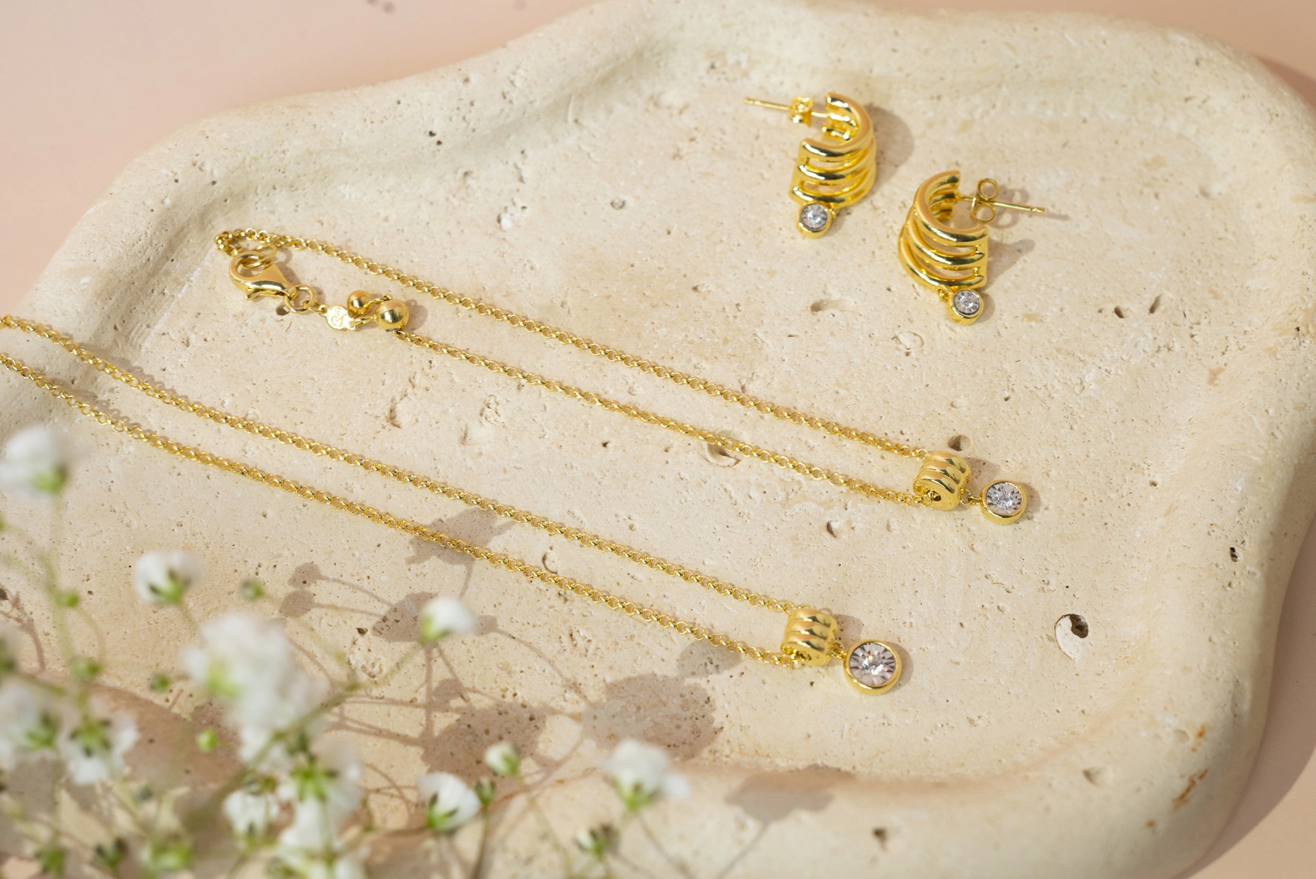 spring product photography of a gold jewelry set on a stone with accent flowers.
