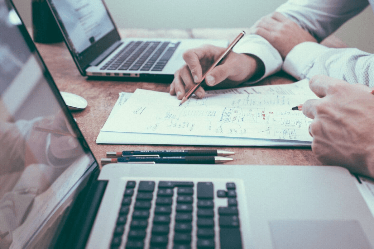Two people working together writing notes down on a piece of paper, with two laptops in front of them.