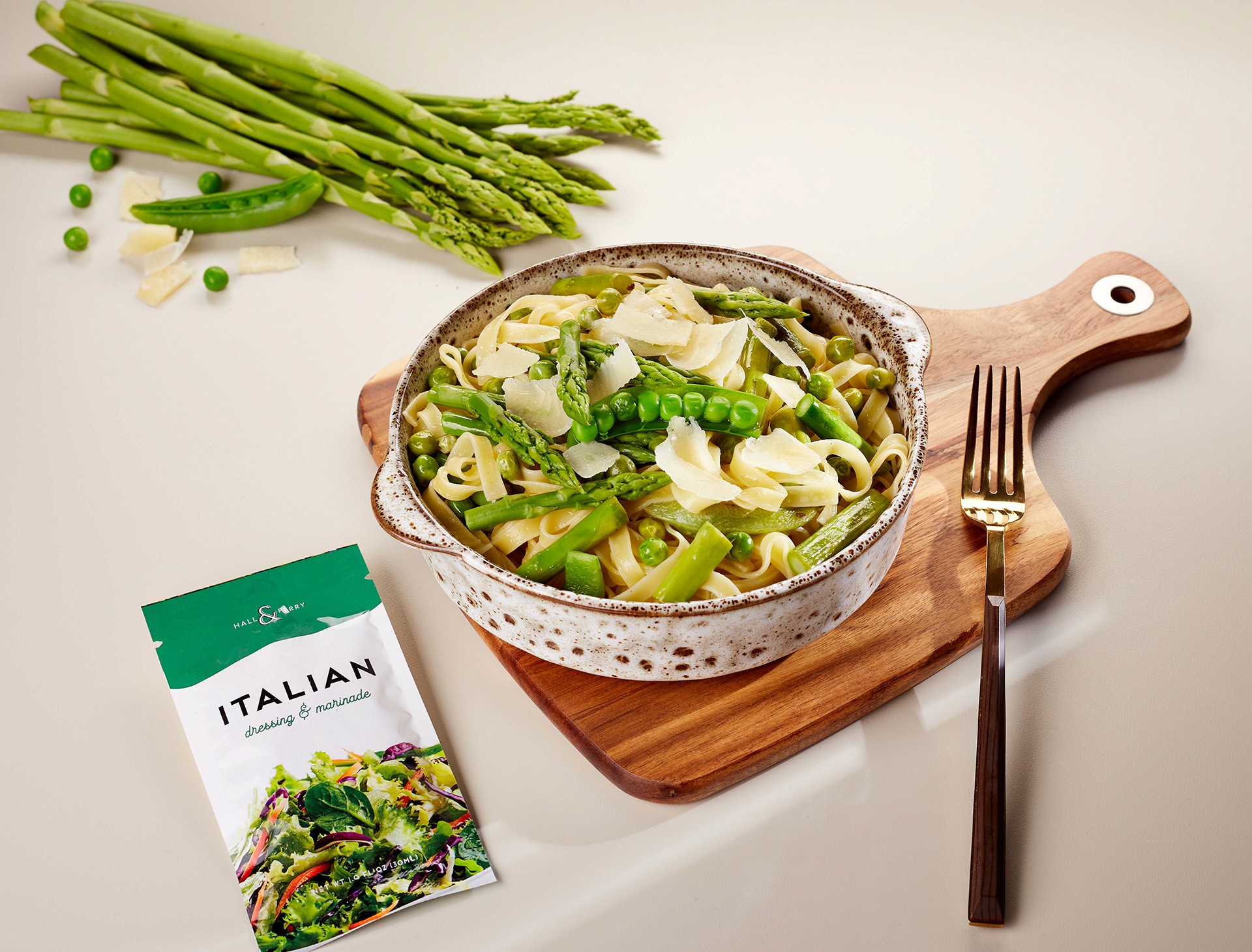 A vibrant bowl of fresh green pasta topped with asparagus and peas, displayed on a wooden cutting board alongside a package of Italian Pocket Flavors seasoning blend.