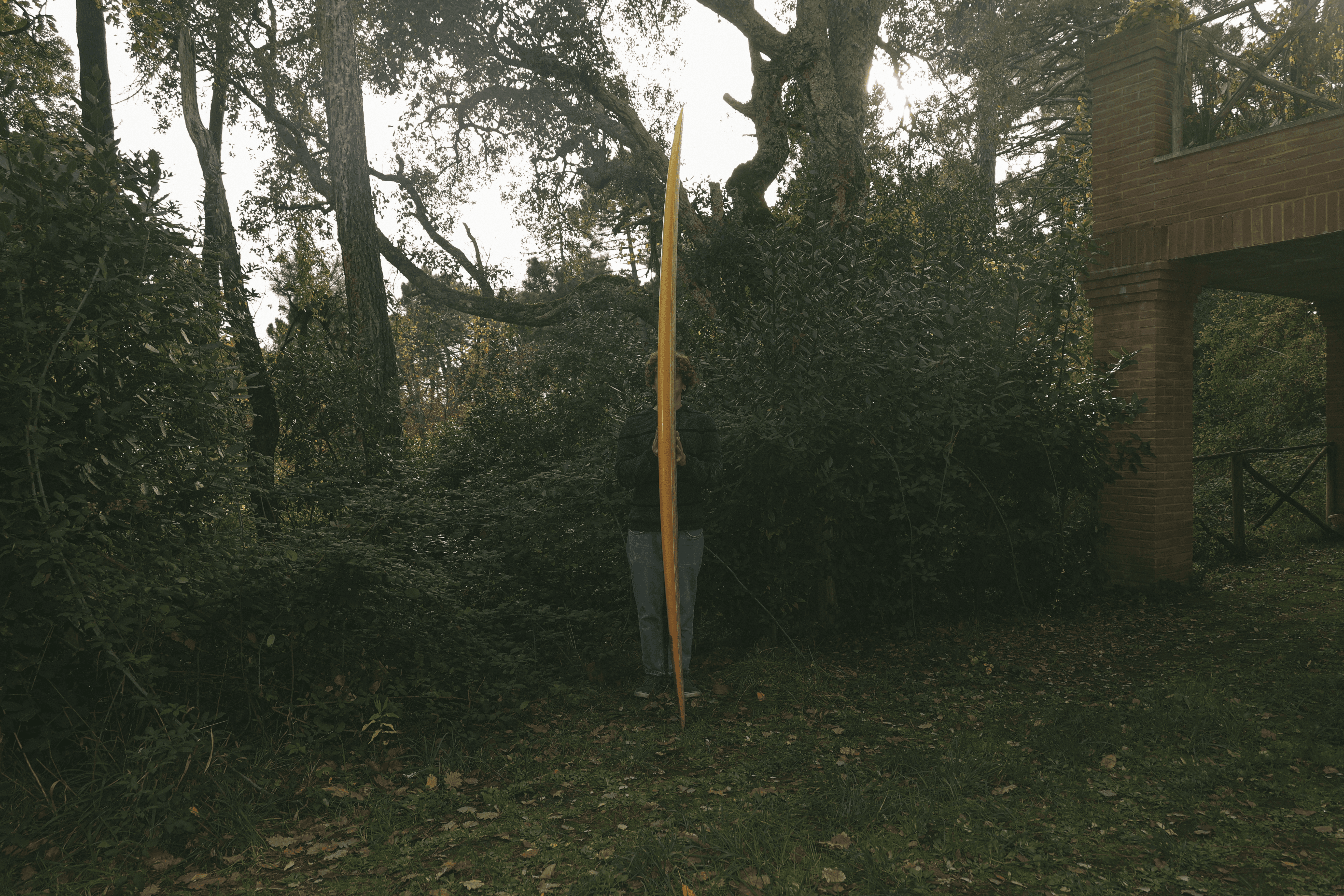 Una persona in piedi, quasi nascosta da una tavola Cavendish che tiene in verticale al centro di un boschetto verde.