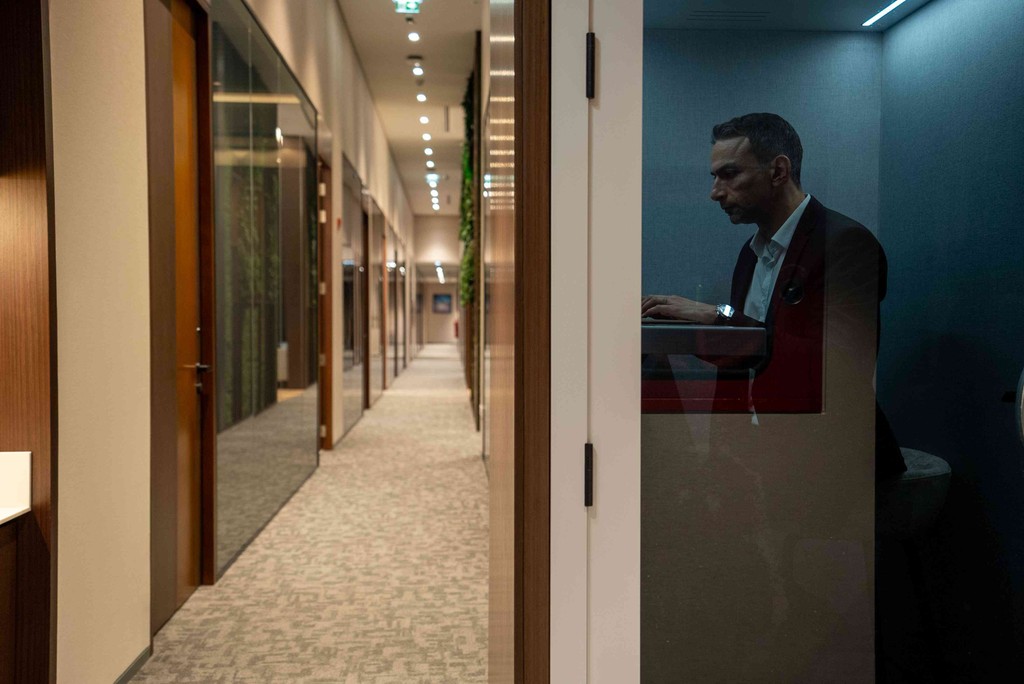 Man in quiet focus pod near well-lit hallway with glass doors in professional virtual offices abu dhabi setting. 