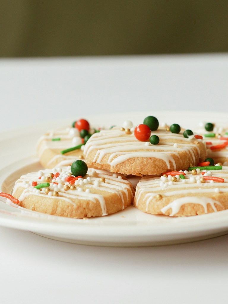 A plate of festive Christmas cookies decorated with icing and colorful sprinkles, showcasing a holiday theme.