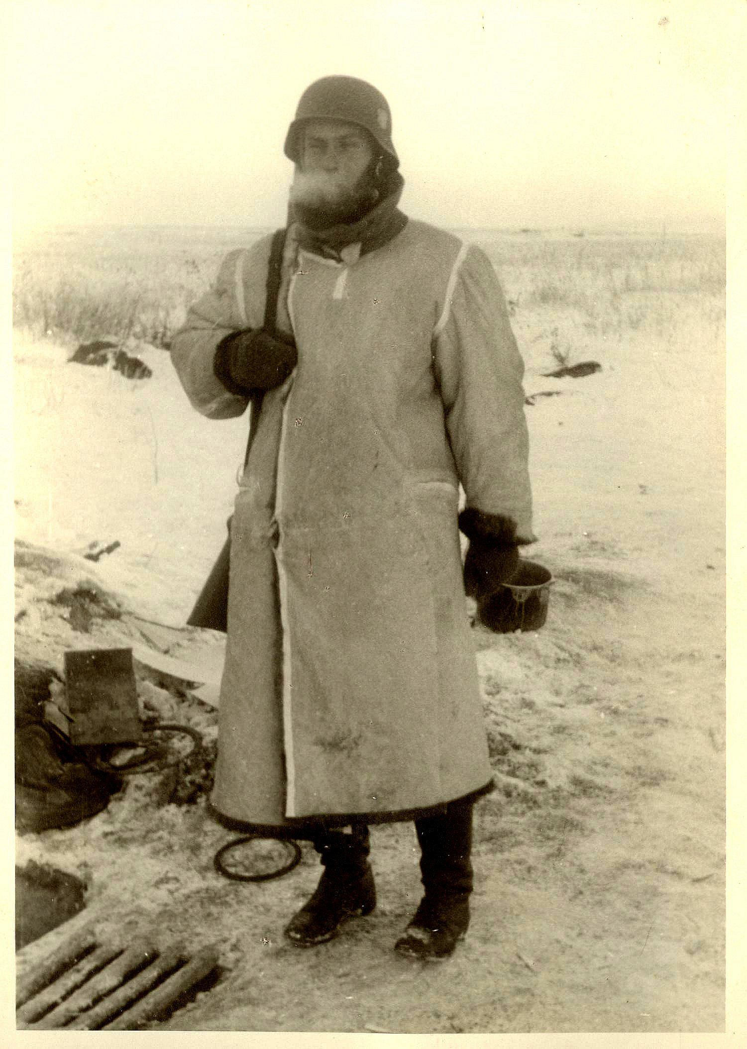 Tysk soldat i vinteruniform står i sneklædt landskab under Anden Verdenskrig. Han bærer en hjelm og en varm frakke, mens kulden er tydelig i det frosne landskab omkring ham.