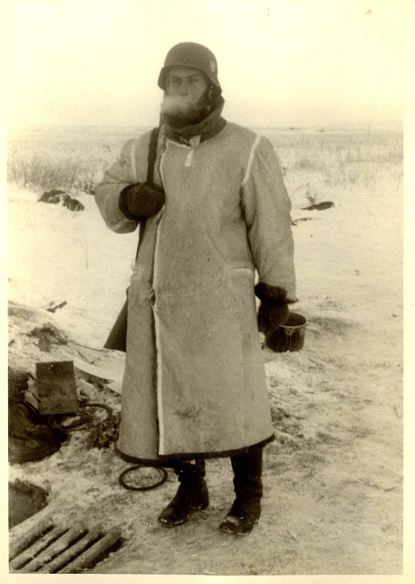 Tysk soldat i vinteruniform står i sneklædt landskab under Anden Verdenskrig. Han bærer en hjelm og en varm frakke, mens kulden er tydelig i det frosne landskab omkring ham.