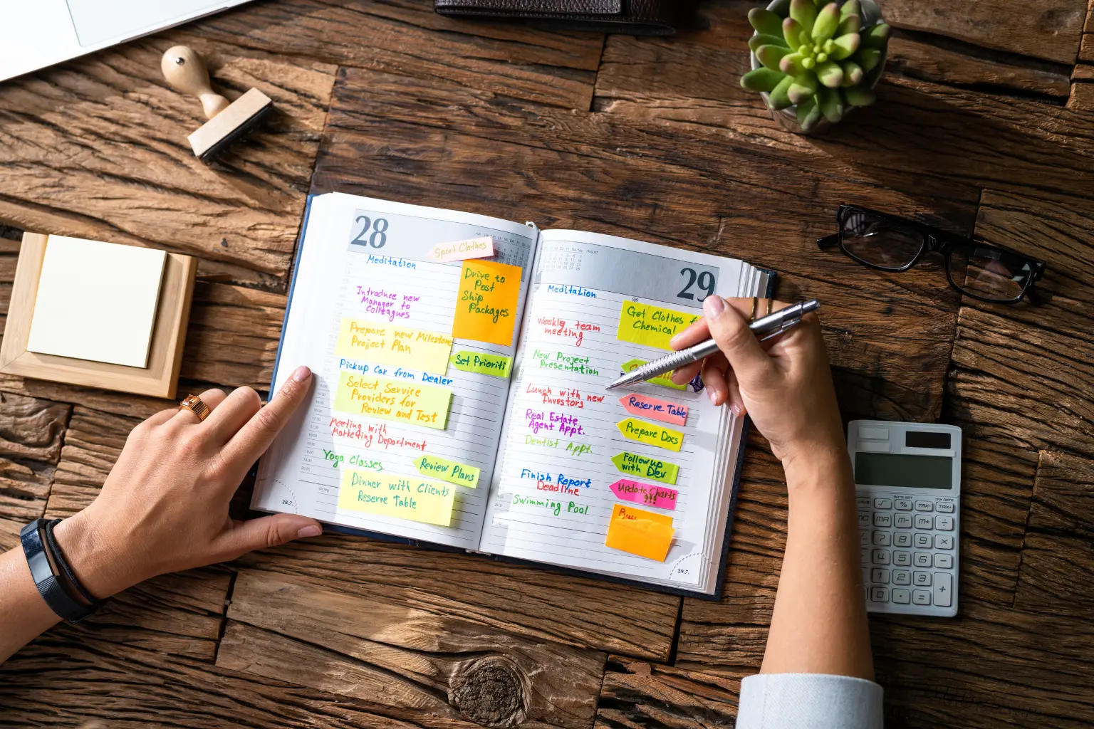 Calendar syncing automation planner filled with colorful sticky notes and tasks on a wooden desk with a calculator.
