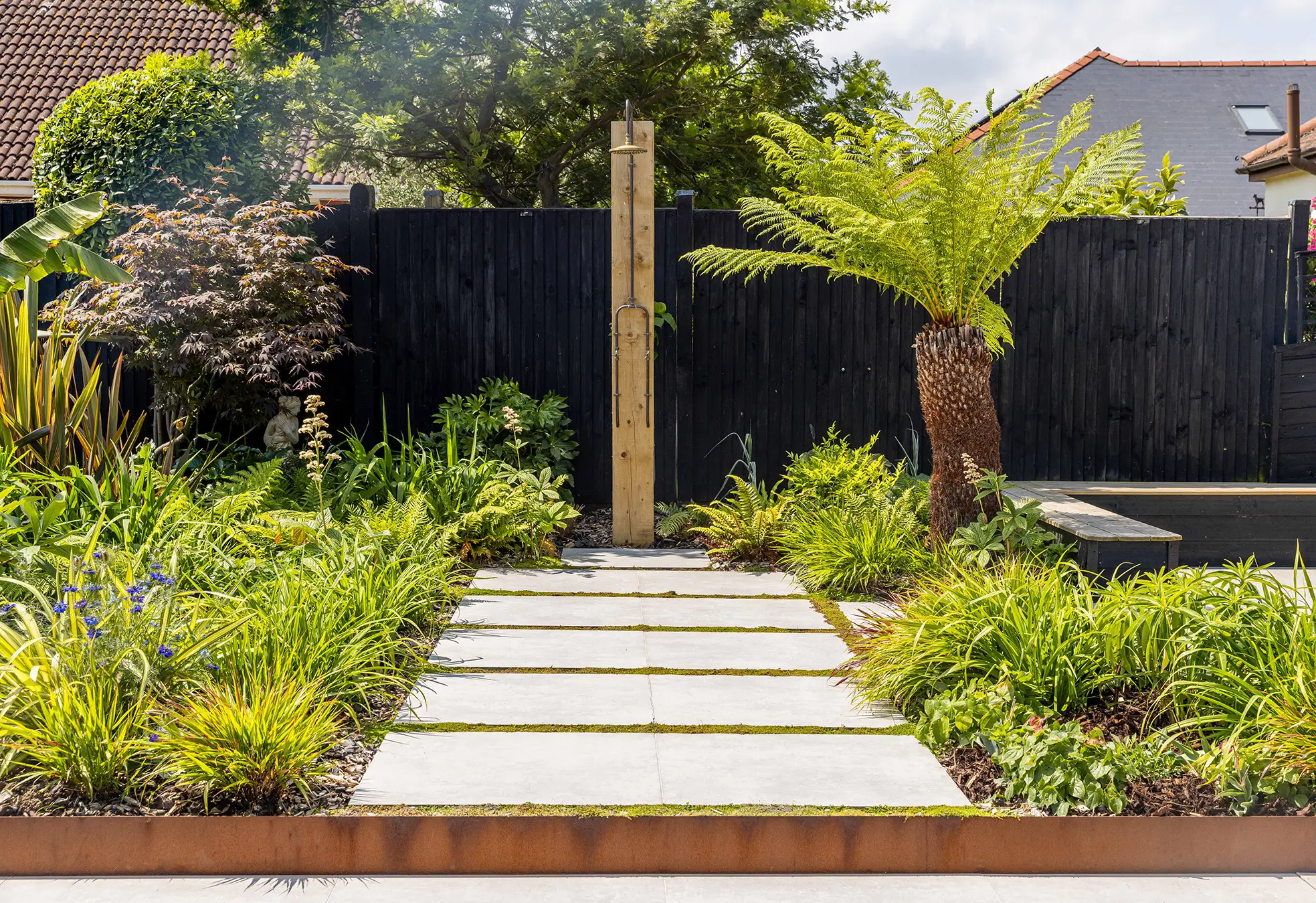 A serene garden pathway leads to a wooden gate, surrounded by lush greenery and decorative plants.