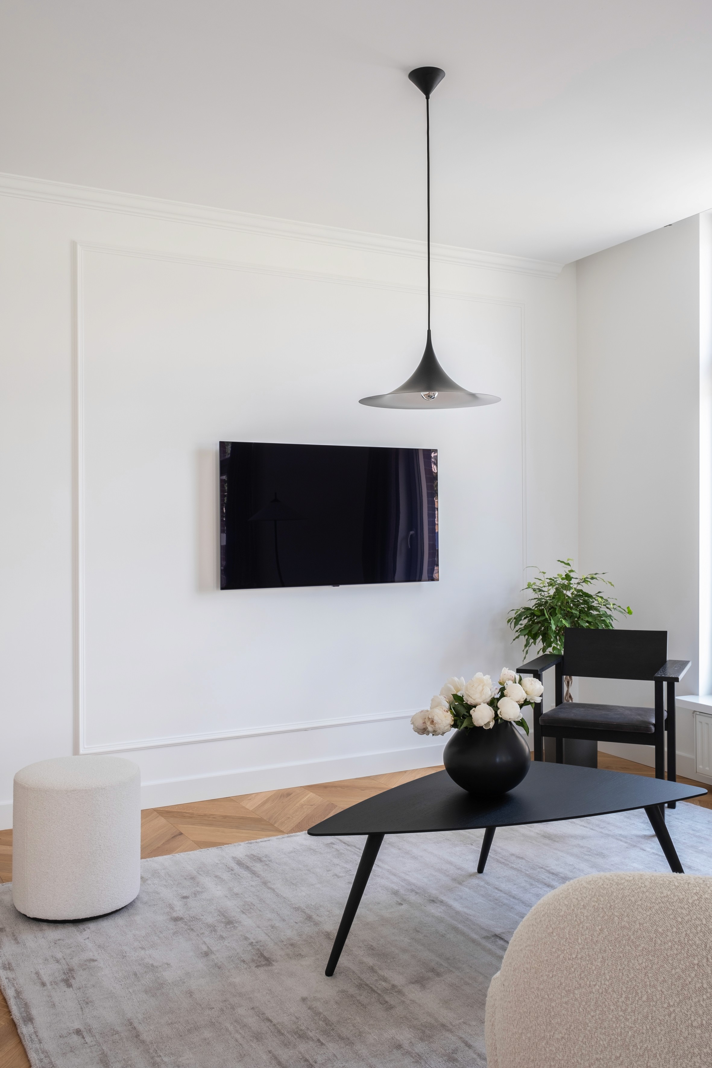 Studio Henk chair, white pouf and coffee table with wall-mounted television, pendant lamp and minimalist styling
