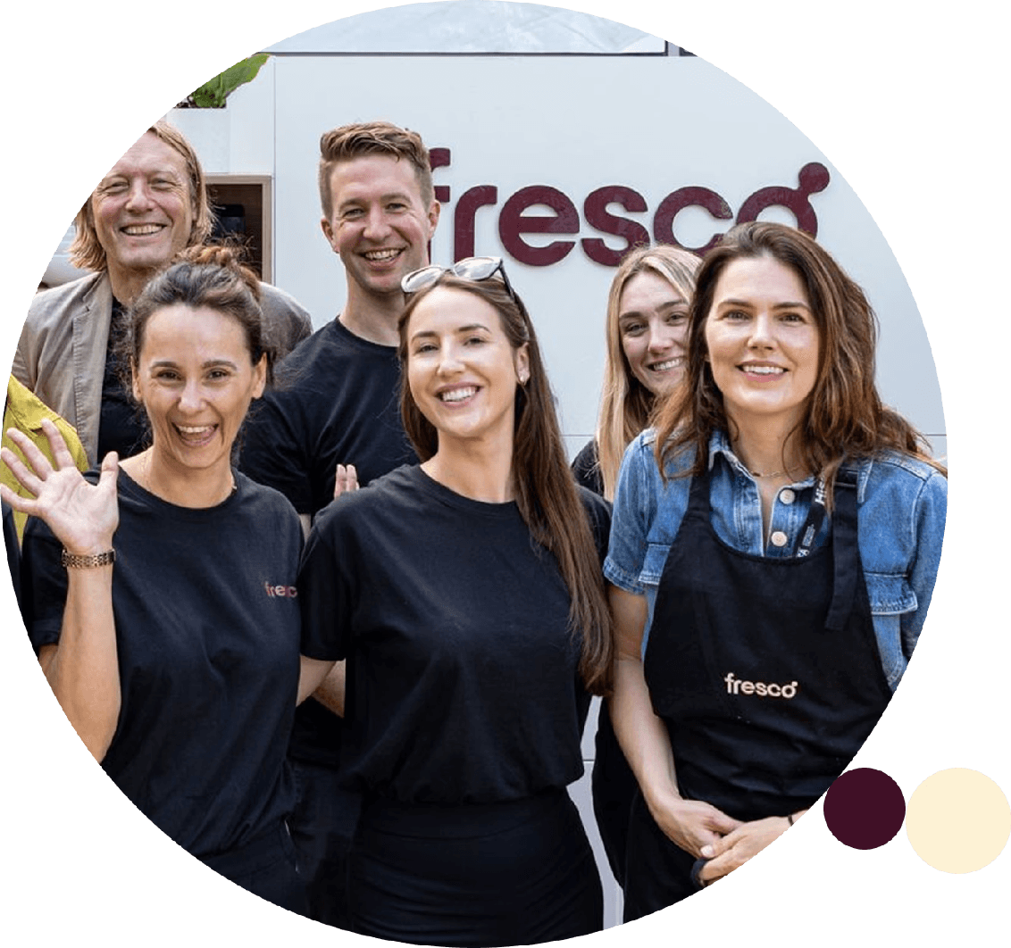 Group of Fresco employees stand together smiling in front of a branded backdrop