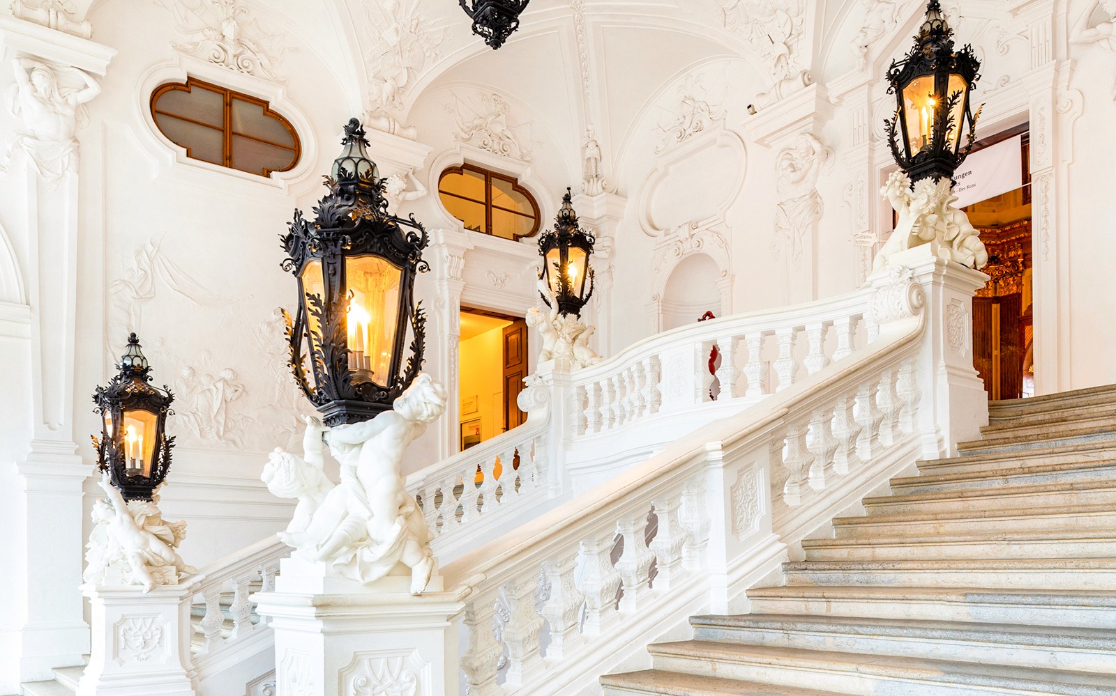 Tangga dalam Istana Belvedere Atas dengan lentera dan patung yang dihias dengan indah.