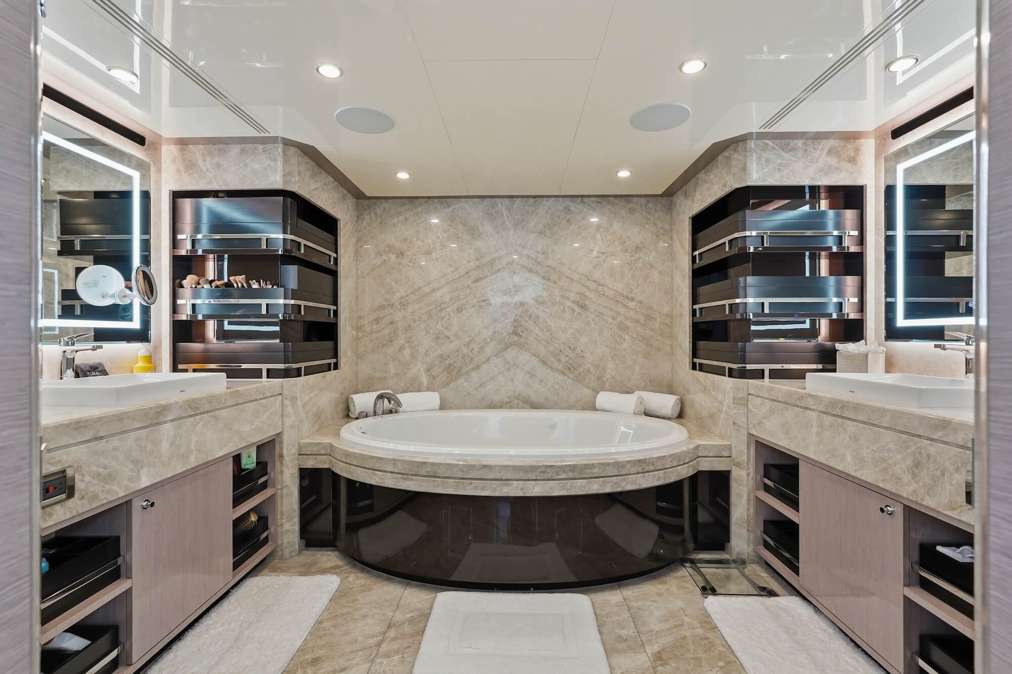 Luxury yacht bathroom with symmetrical vanities, illuminated mirrors, marble finishes, custom storage, and a central soaking tub.