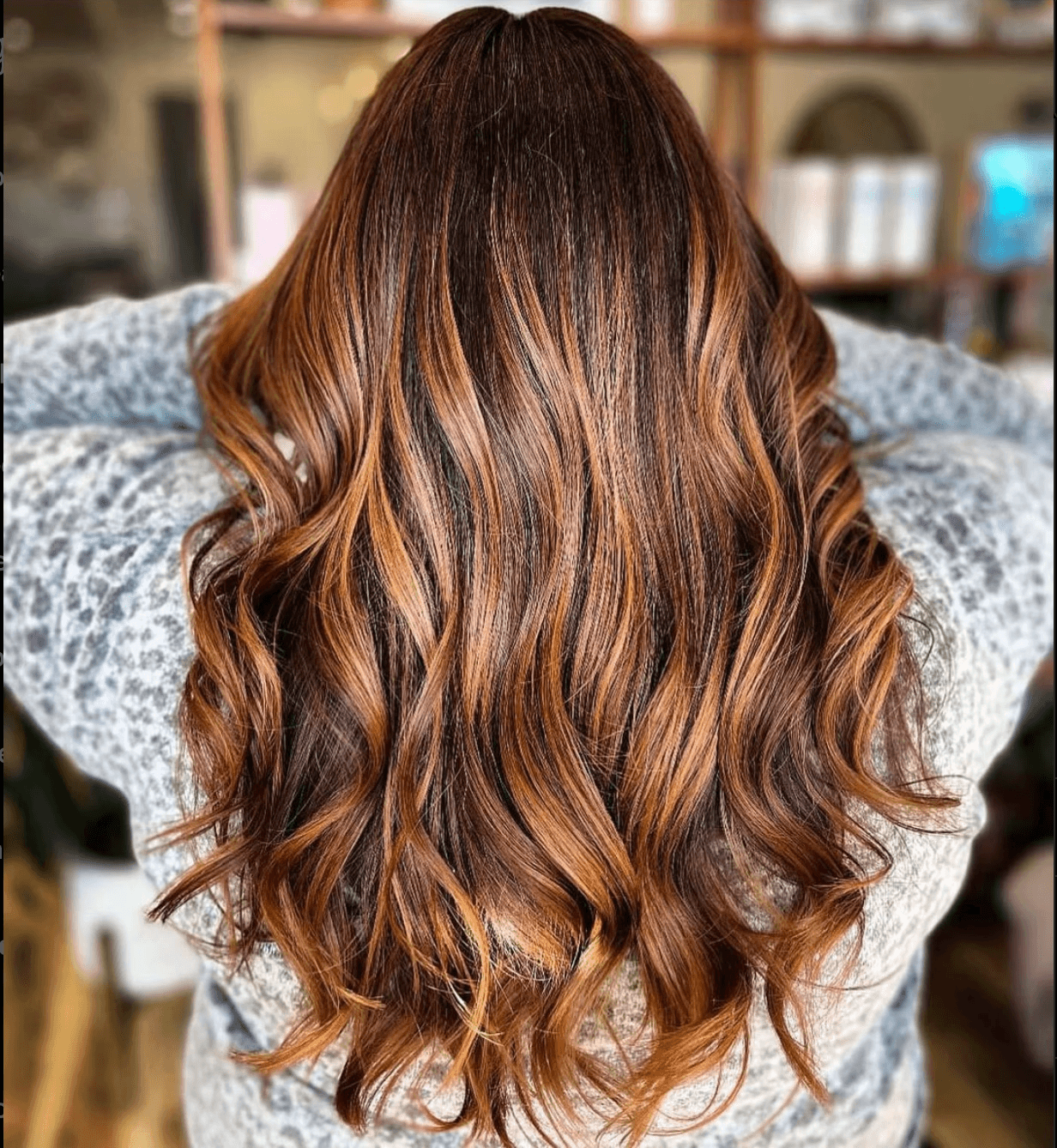 Back view of long, copper brunette hair with dimensional caramel highlights, styled in soft beachy waves for a warm, radiant finish.